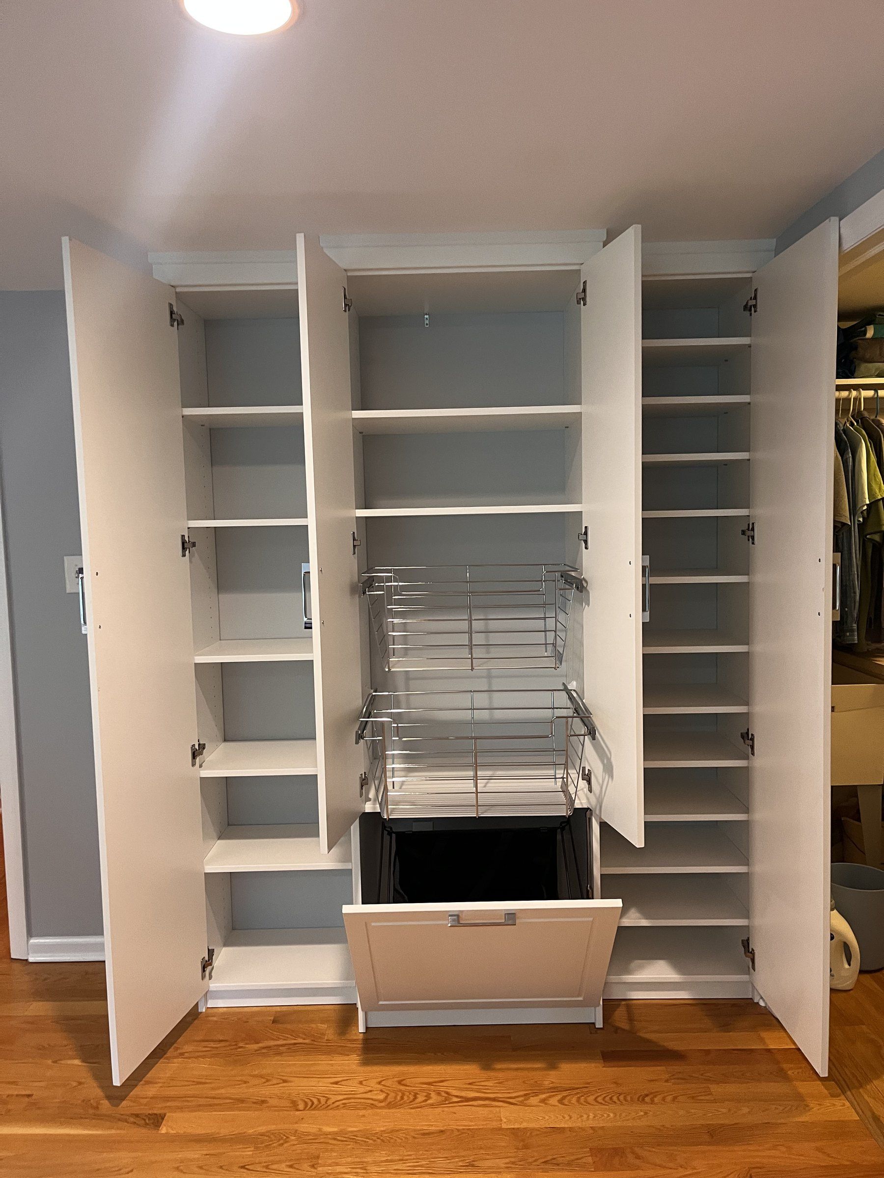 White closet cabinet open to show a pull-out wire basket and tilt-out hamper
