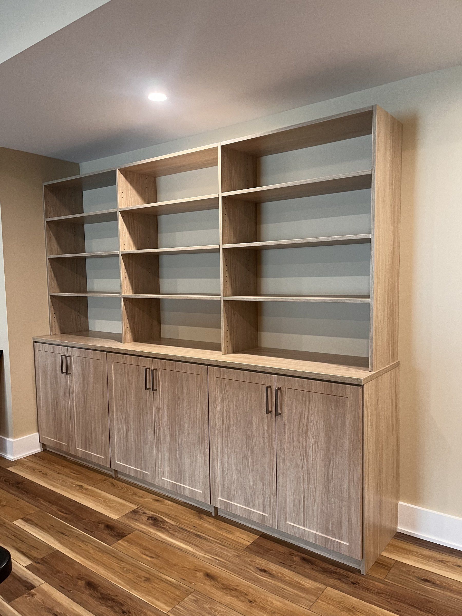 Light wood built-in shelving wall with closed lower cabinets