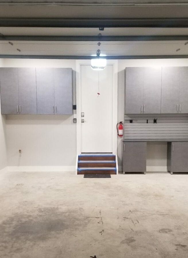 Garage with upper wall cabinets over two workbenches by the house door