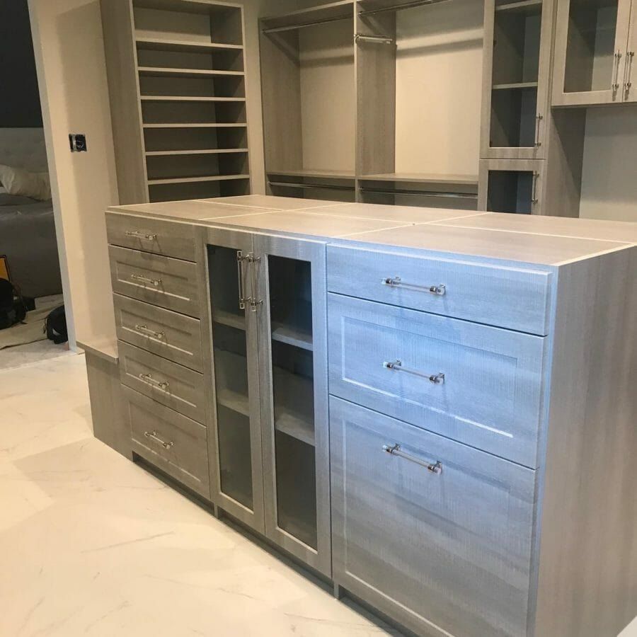 Gray walk-in closet island with glass-front upper cabinets