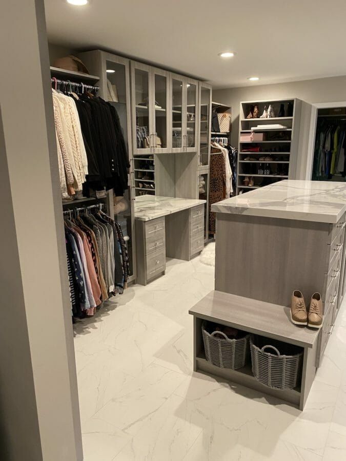 Gray walk-in closet with an island and bench over a marble floor