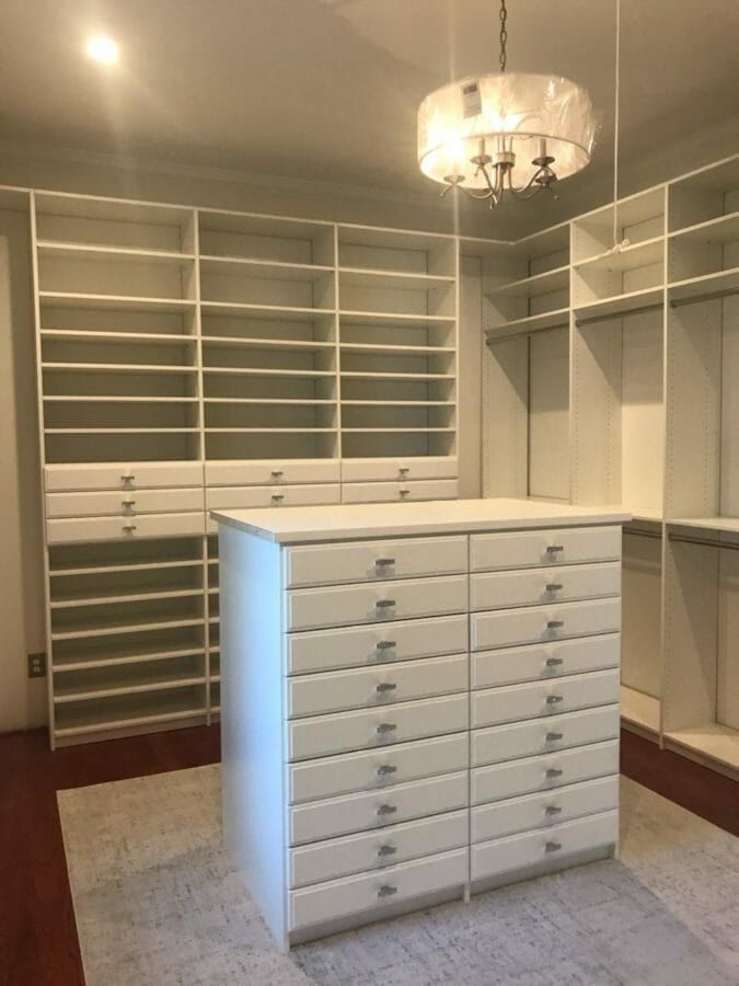 Walk-in closet with a white drawer island under a chandelier
